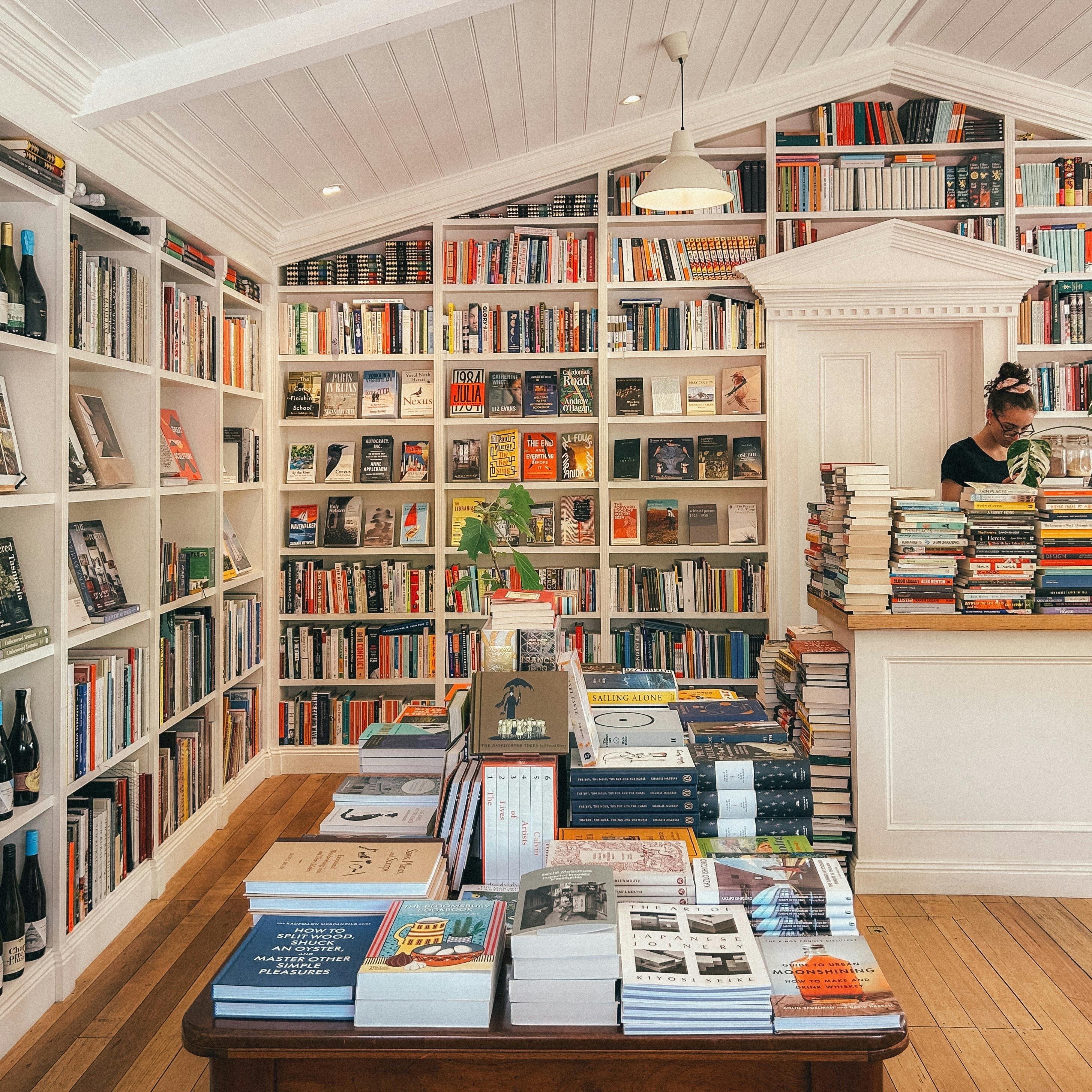 Interior of a bookshop with shelves of books and a central table stacked with titles.