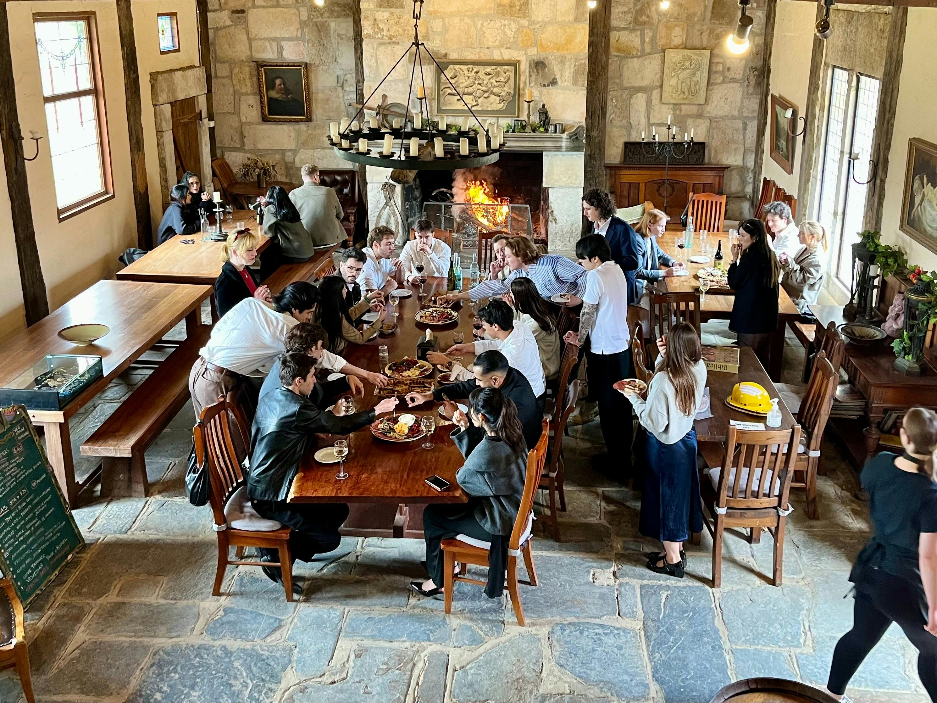 group of people enjoying food and wine at tables in front of a fireplace