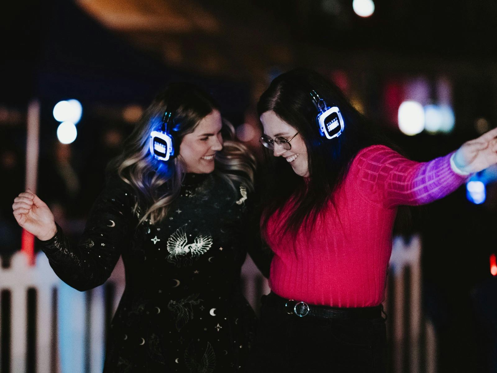 Two people wearing glowing headphones dancing at a night silent disco.