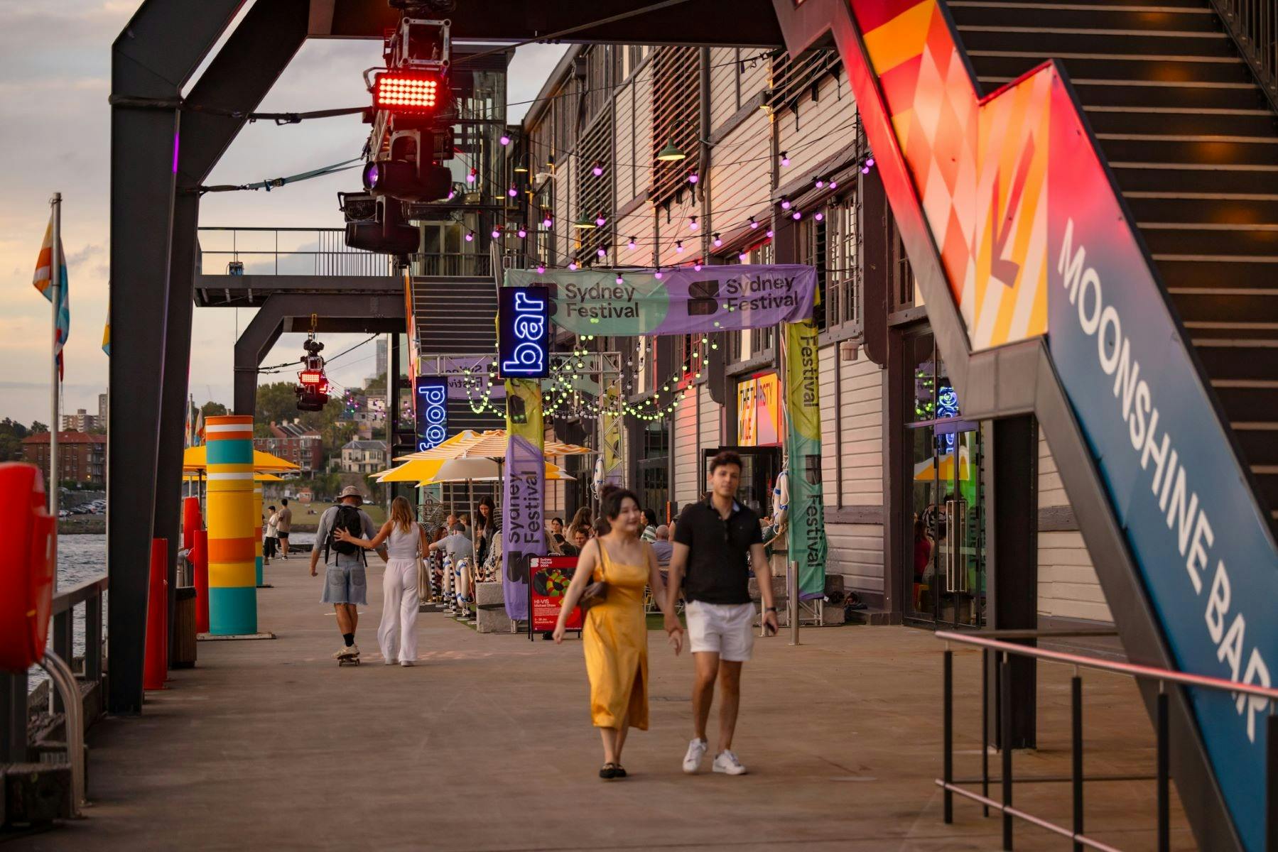 Two people walking along a sidewalk adjacent to a building displaying an array of colorful signs.