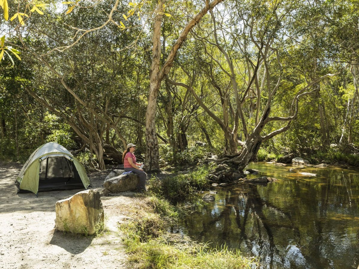 Person sitting on rock looking at creek with a tent set up behind them.