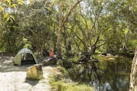 Person sitting on rock looking at creek with a tent set up behind them.