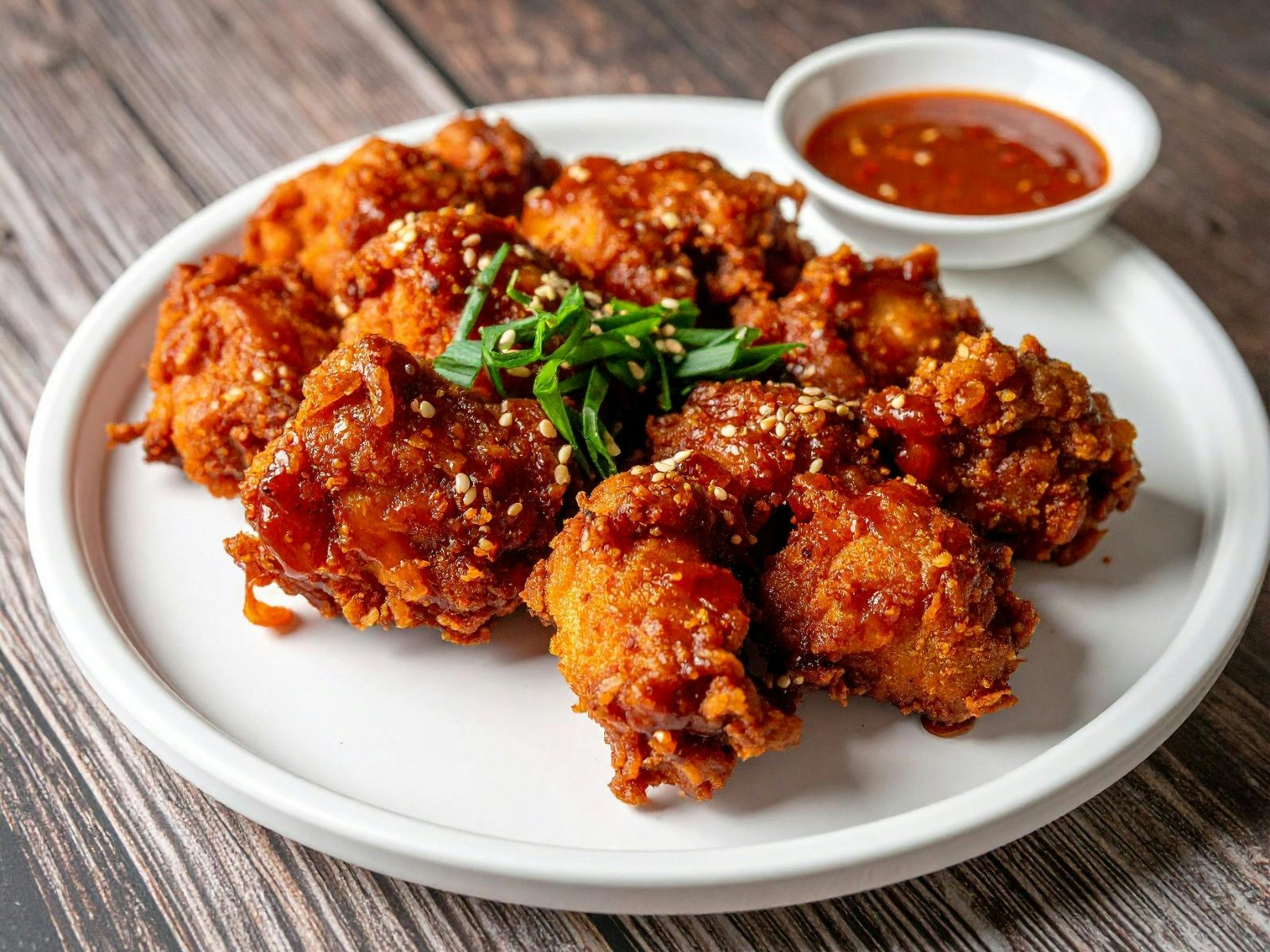 Served on a white platter is crispy fried chicken with a side dish of dipping sauce.
