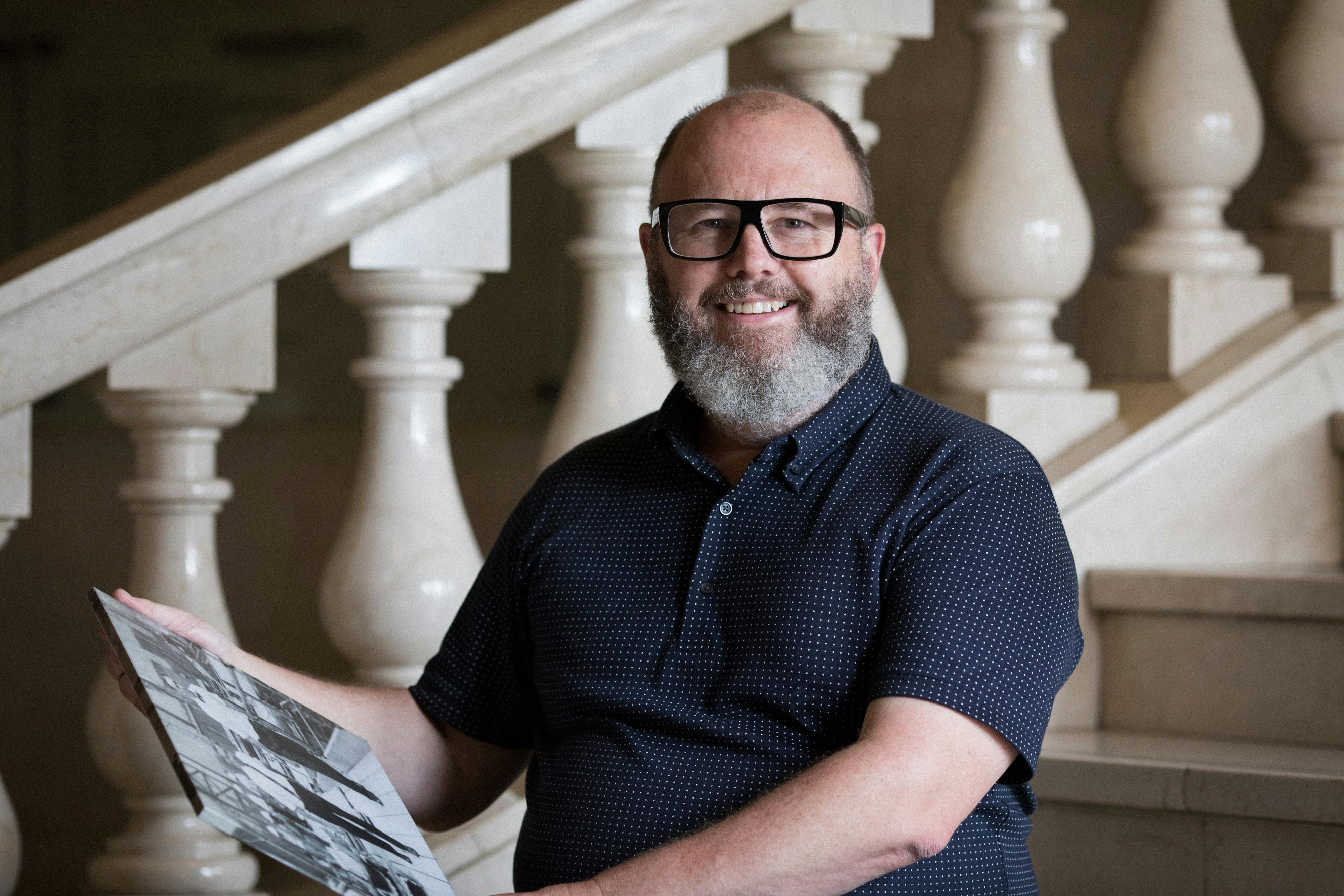 A man smiling on a marble staircase holding a black and white photograph