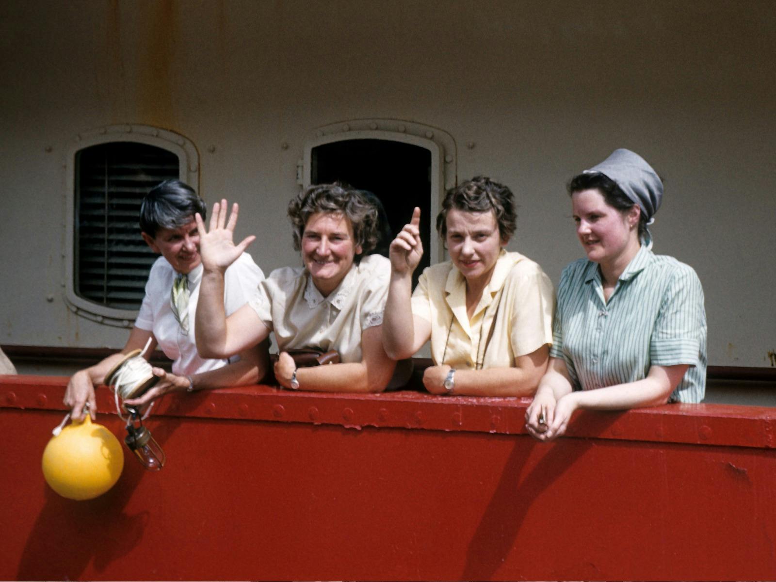 Four women smiling and waving on a boat.