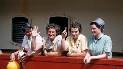 Four women smiling and waving on a boat.