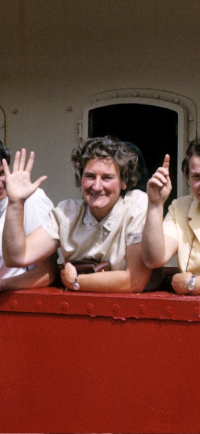 Four women smiling and waving on a boat.