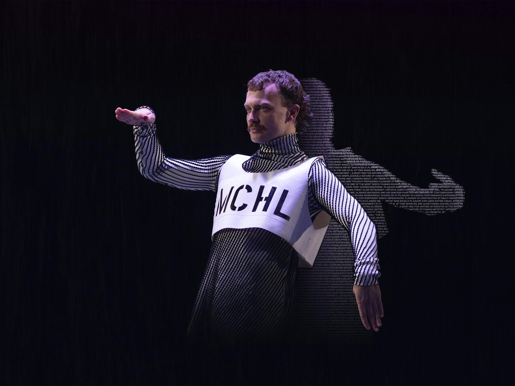 A male dancer poses in a robotic position. His shadow is filled with coloured text. A male dancer poses in a robotic position. His shadow is filled with coloured text.