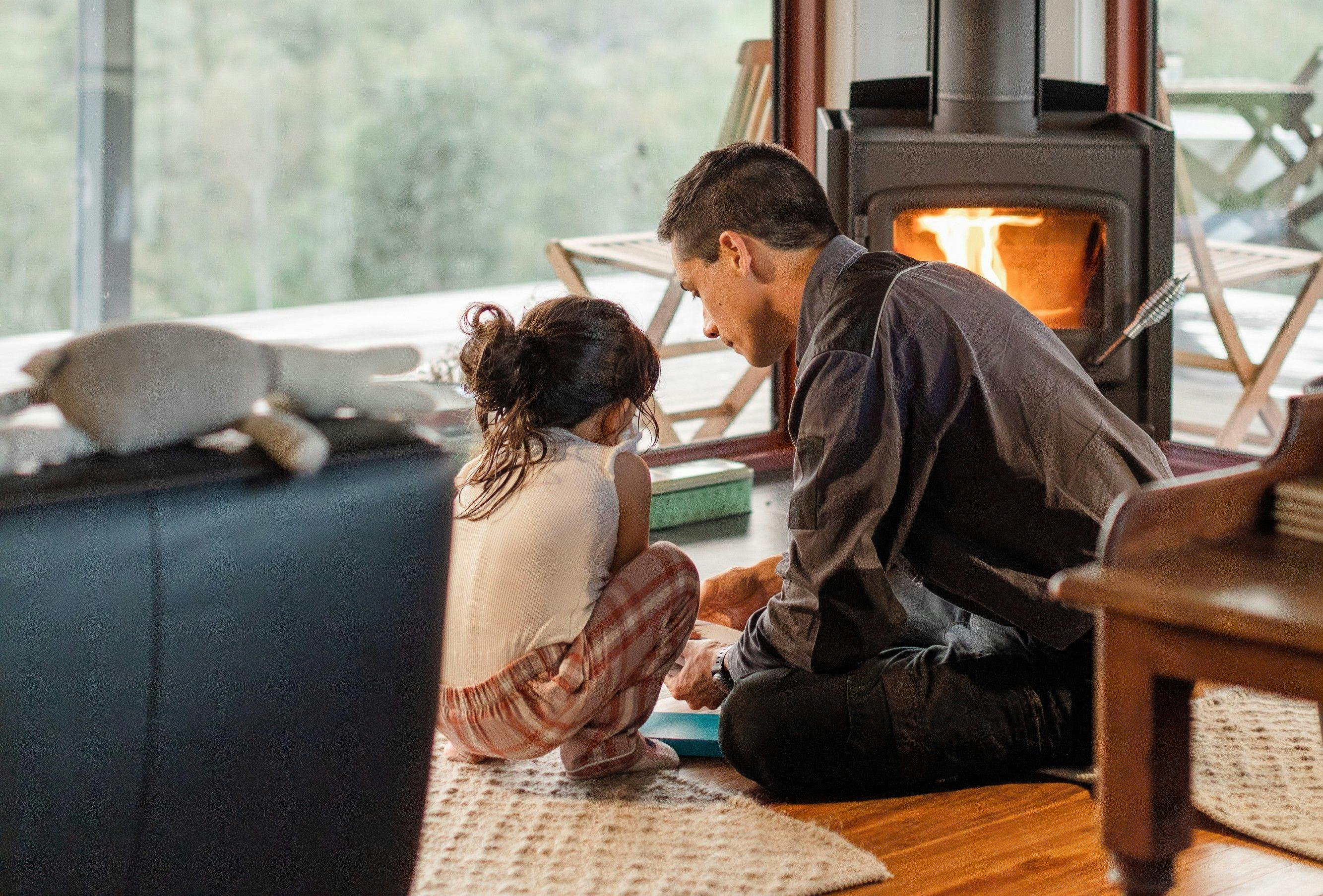 父と娘が暖炉の前で読書をしている。大きな窓からは外の景色が見える。
