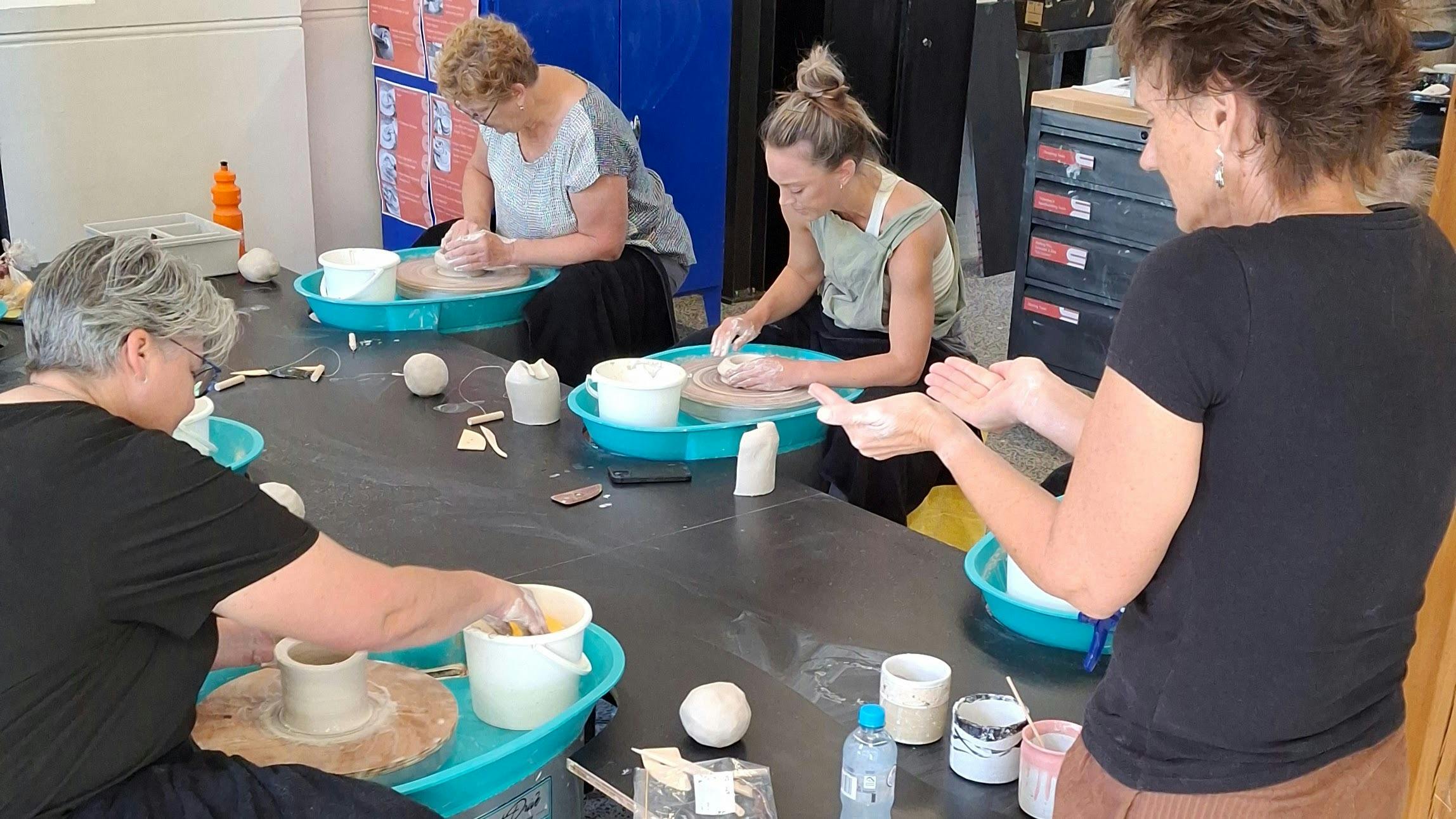 People working on makeing posts on pottery wheels with an instructor describing a shape