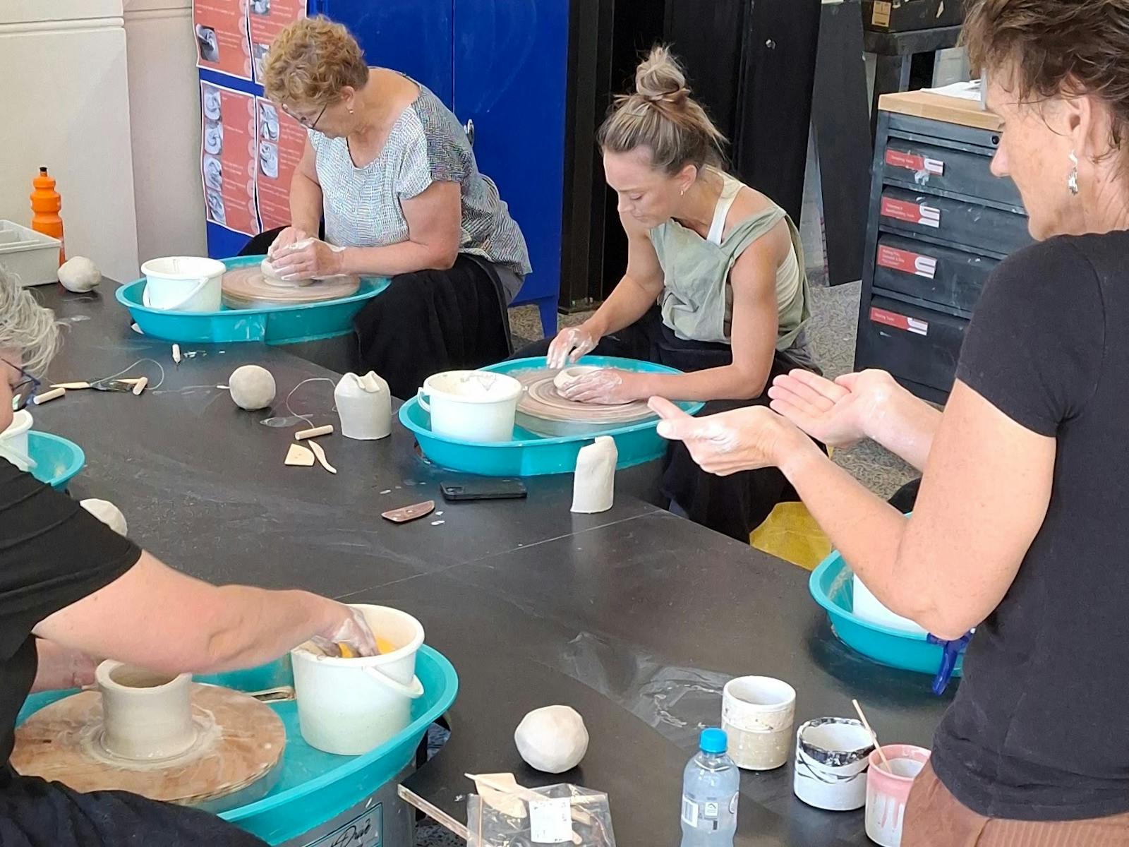 People working on makeing posts on pottery wheels with an instructor describing a shape