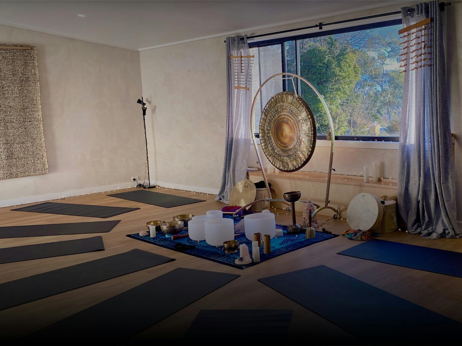 Room set up for a sound bath - singing bowls, gong, drum surrounded by yoga mats on floor.