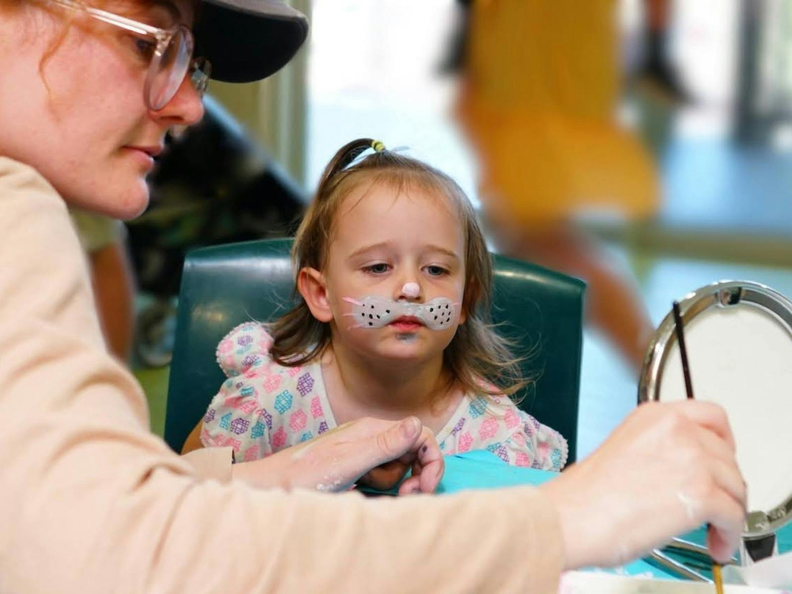 Child having her face painted with bunny print