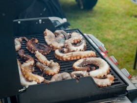 BBQ filled with large octopus tentacles grilling.