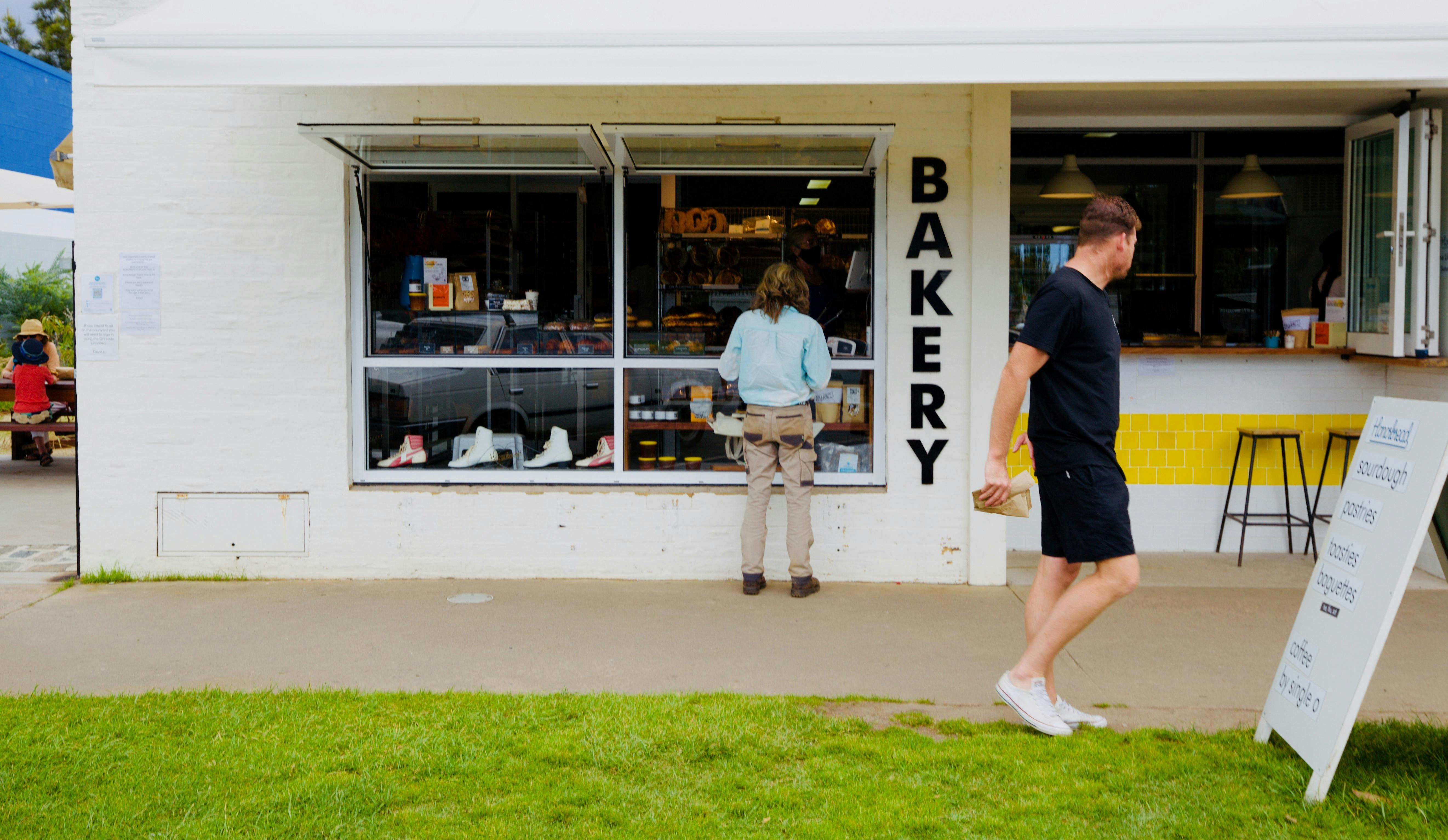 Bakery shopfront with woman at the counter and man walking away with bag in hand