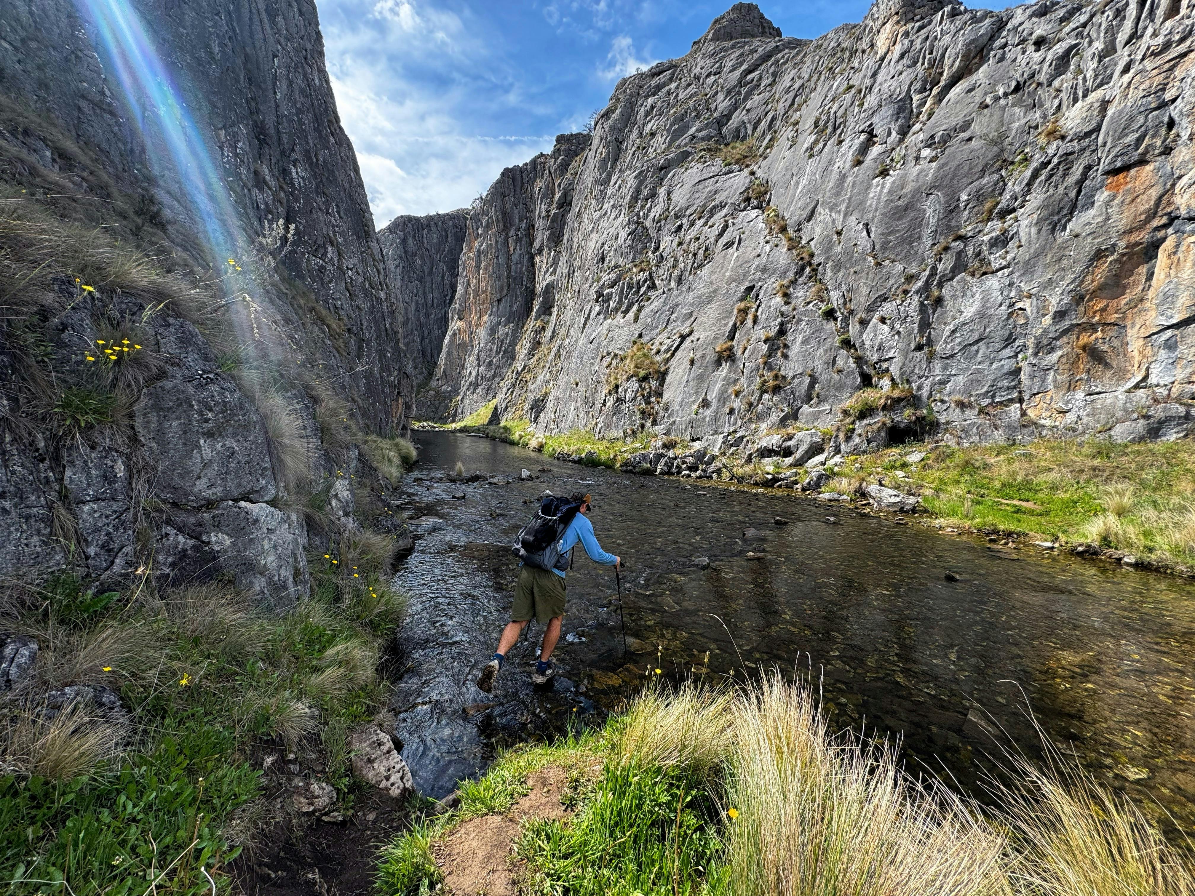 A hiker hopping across some rocks to cross a river in a gorge.