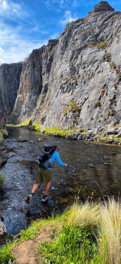 A hiker hopping across some rocks to cross a river in a gorge.