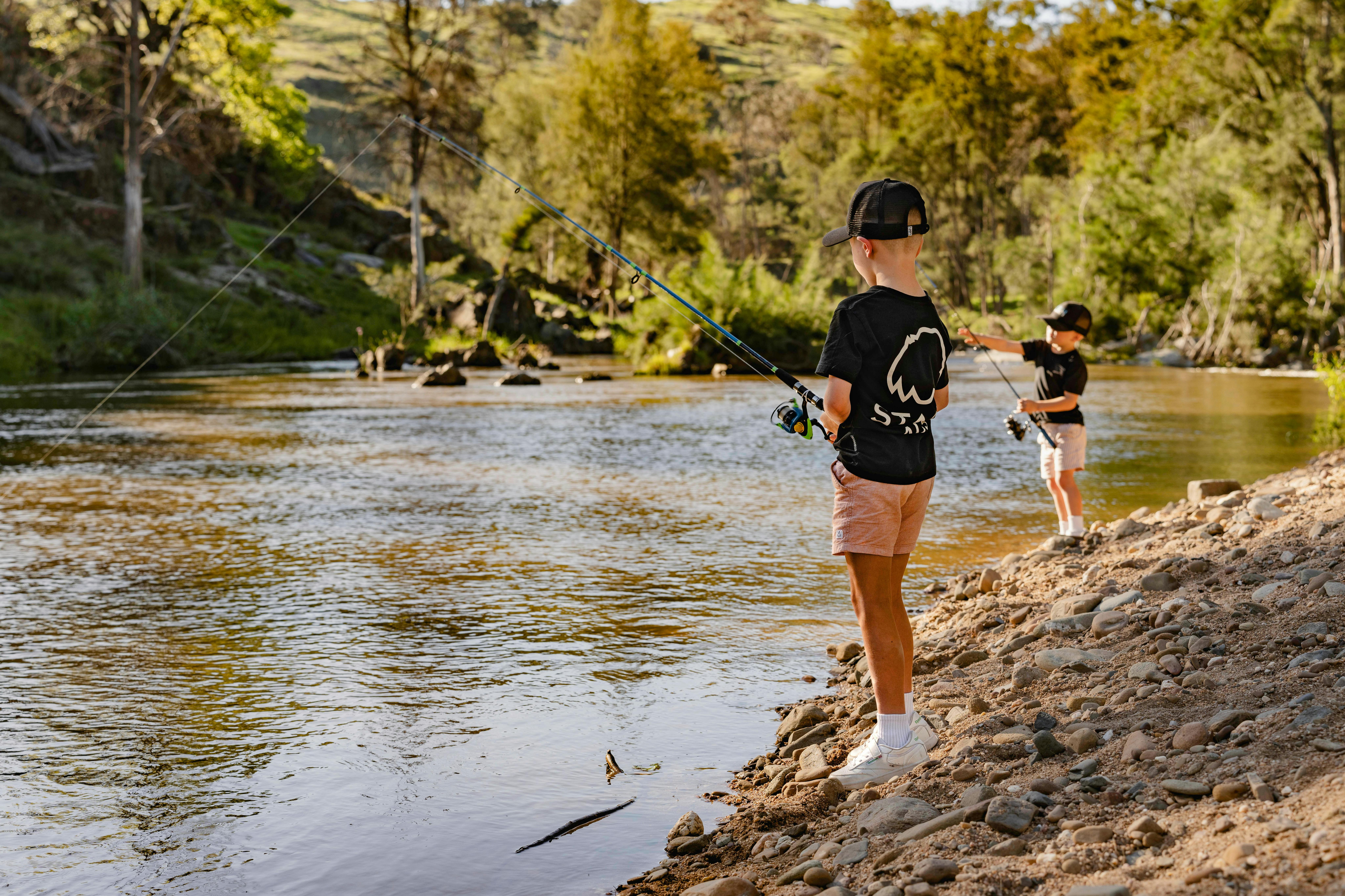 two young boys are fishing on a sandy riverbank
