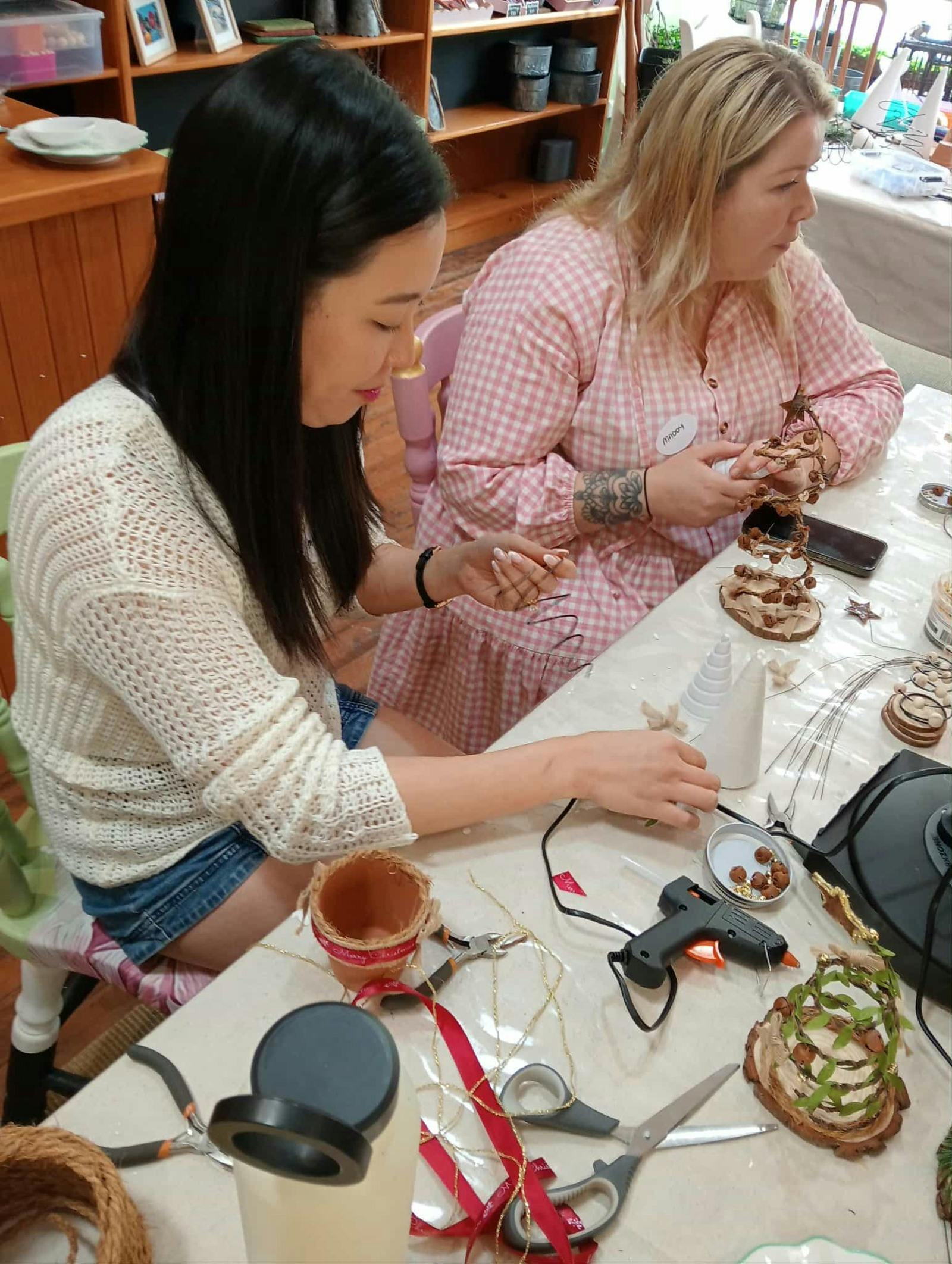 2 women sitting side by side at a work table making their Christmas Wire trees.