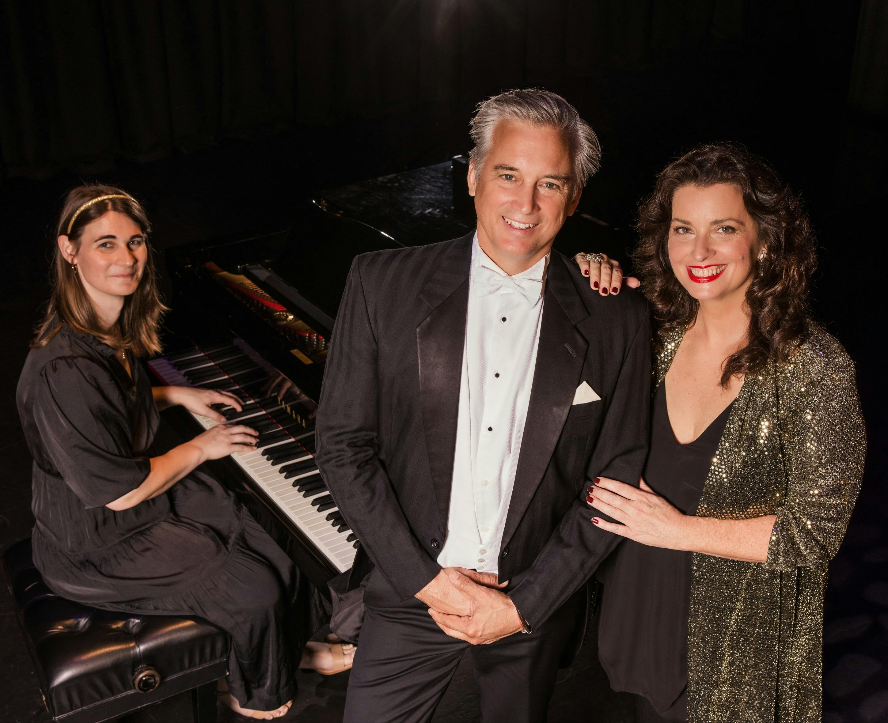 three people sit around a piano