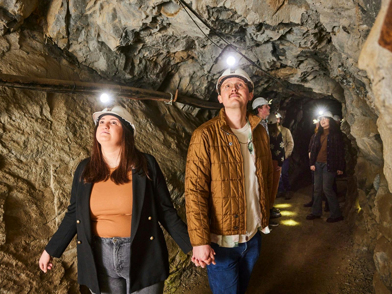 a young woman is holding hands with a taller young gentleman. They are underground in a tunnel.