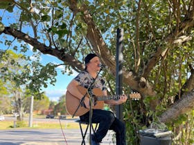 Male Singer holding a guitar, under a tree