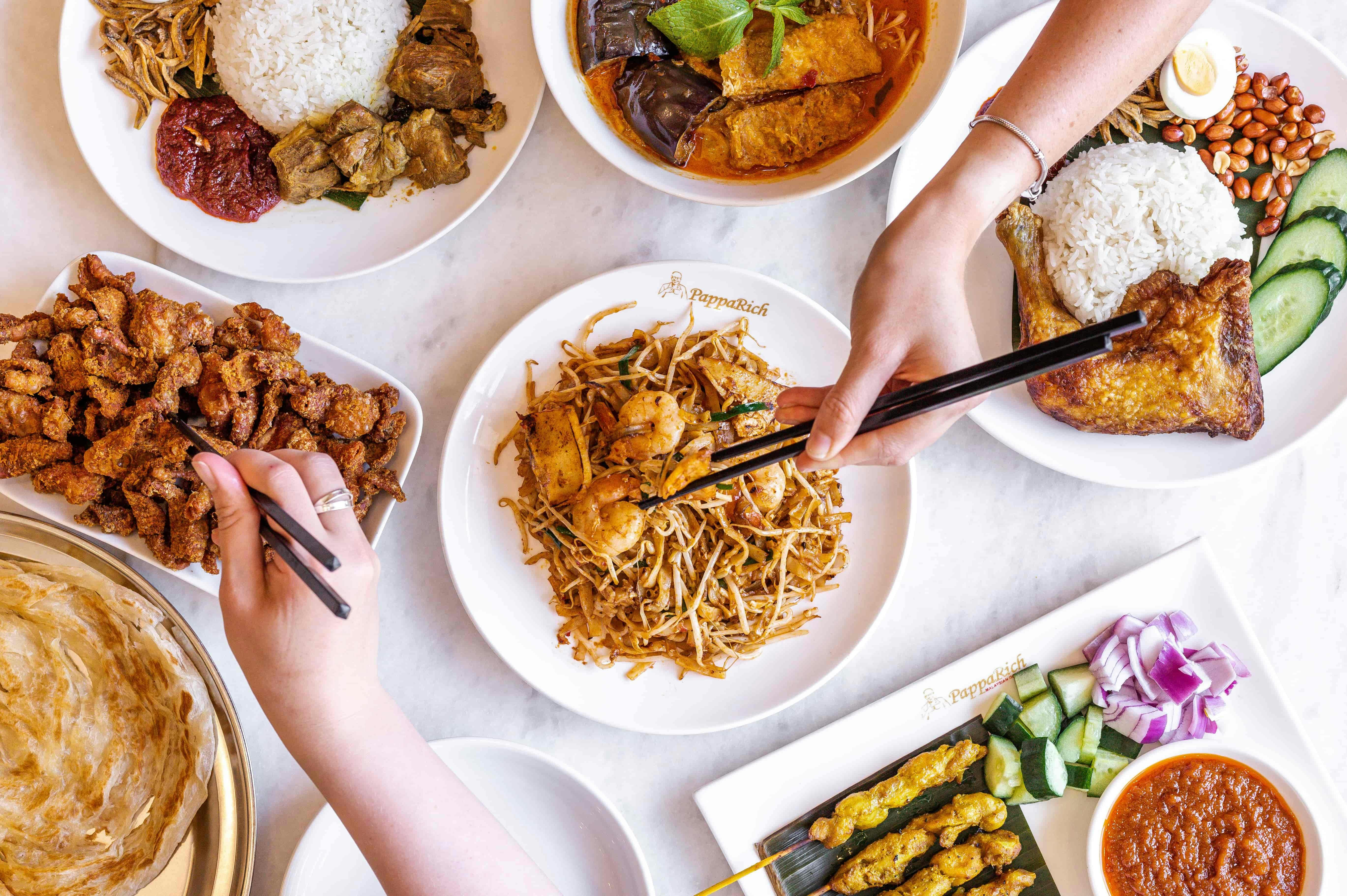 Foto eines Tisches mit viel Essen und Menschen, die mit Stäbchen essen