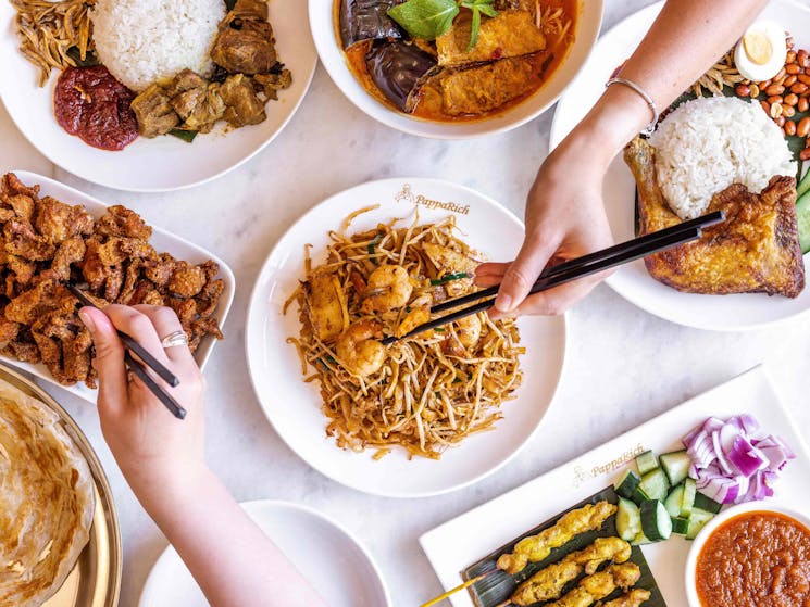 Photo of table with lots of food and people eating with chopsticks