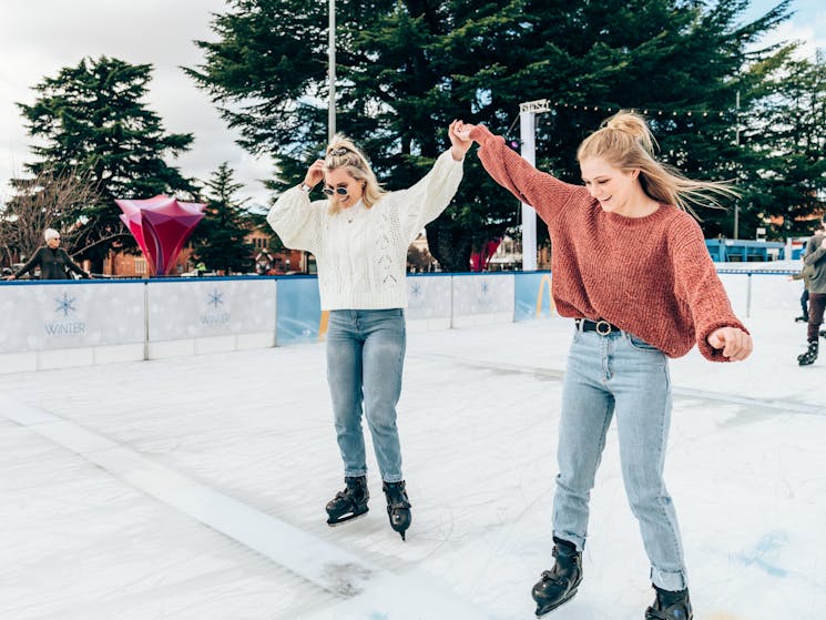 Two ladies ice skating during the day holding hands.