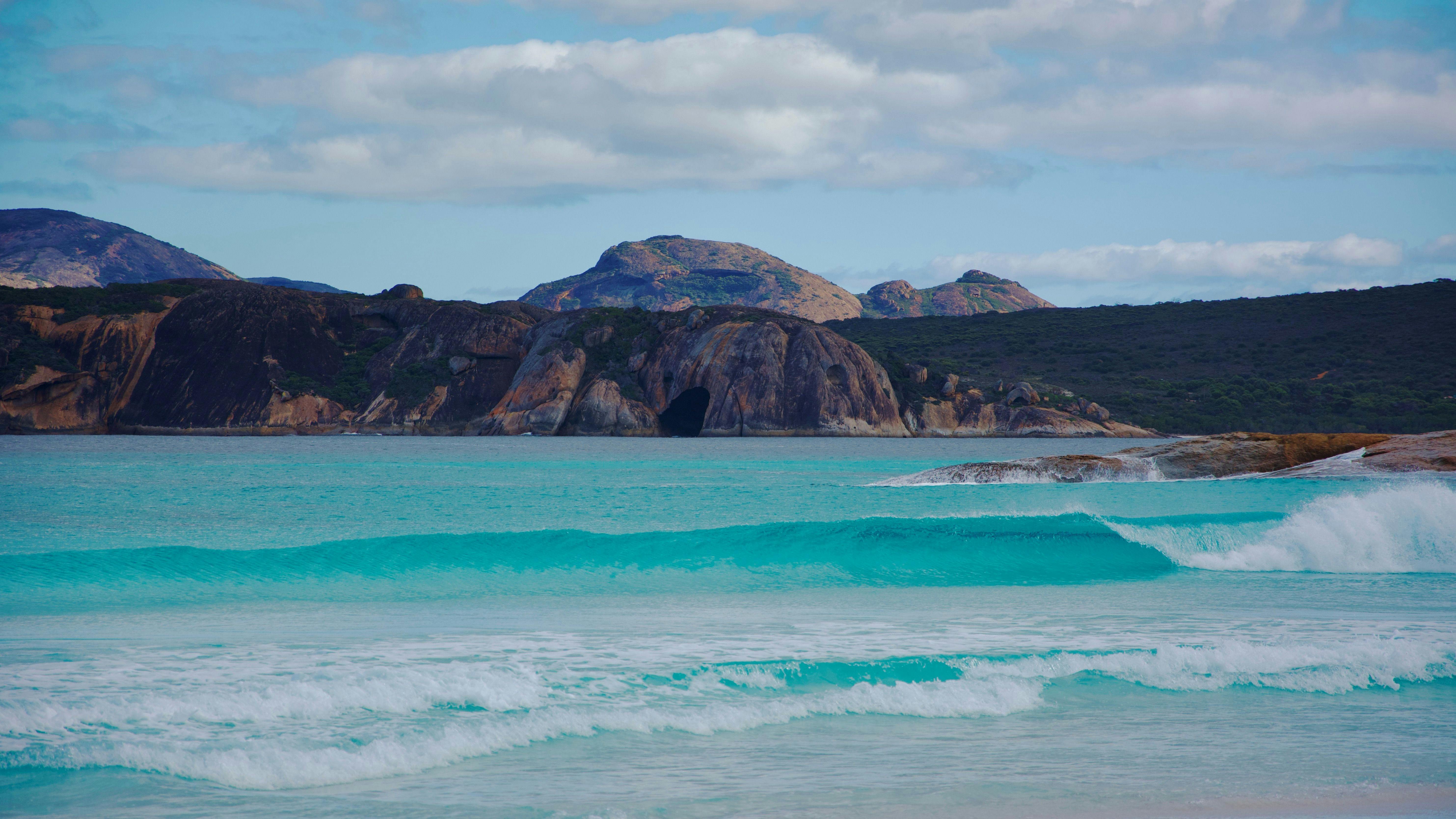 View from beach across to headland, wave peeling in the foreground.