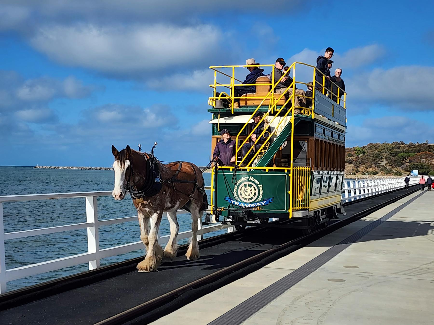 Victor Harbor horse-drawn tram with people standing on the top and Granite Island in the background