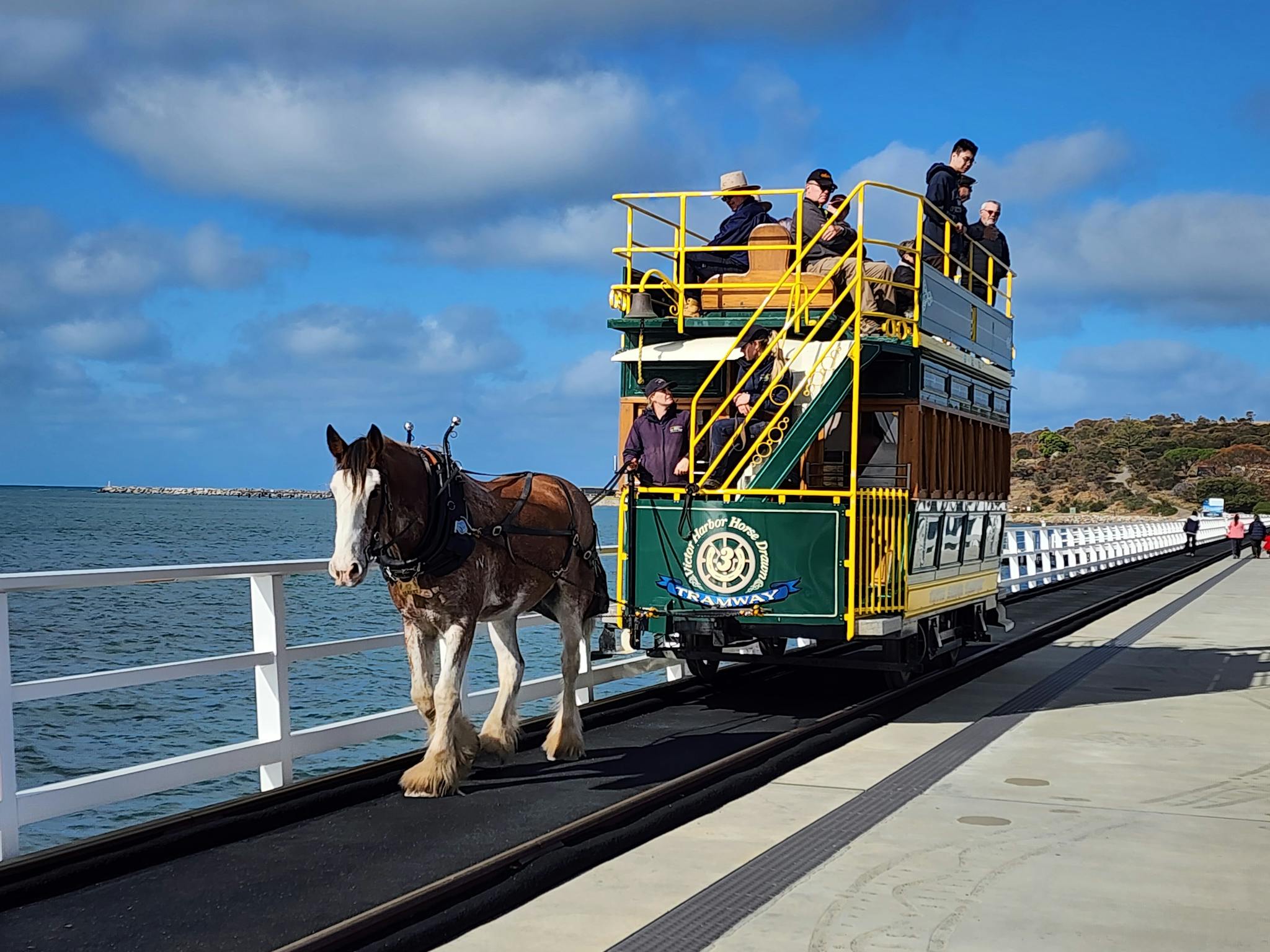 Victor Harbor horse-drawn tram with people standing on the top and Granite Island in the background