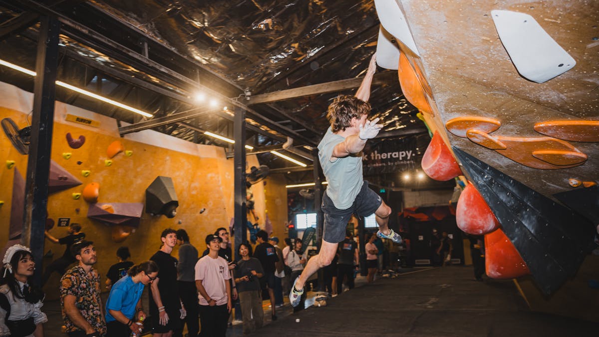 Multiple climbers spectating a male climber just holding onto a swinging dynamic climb with one hand