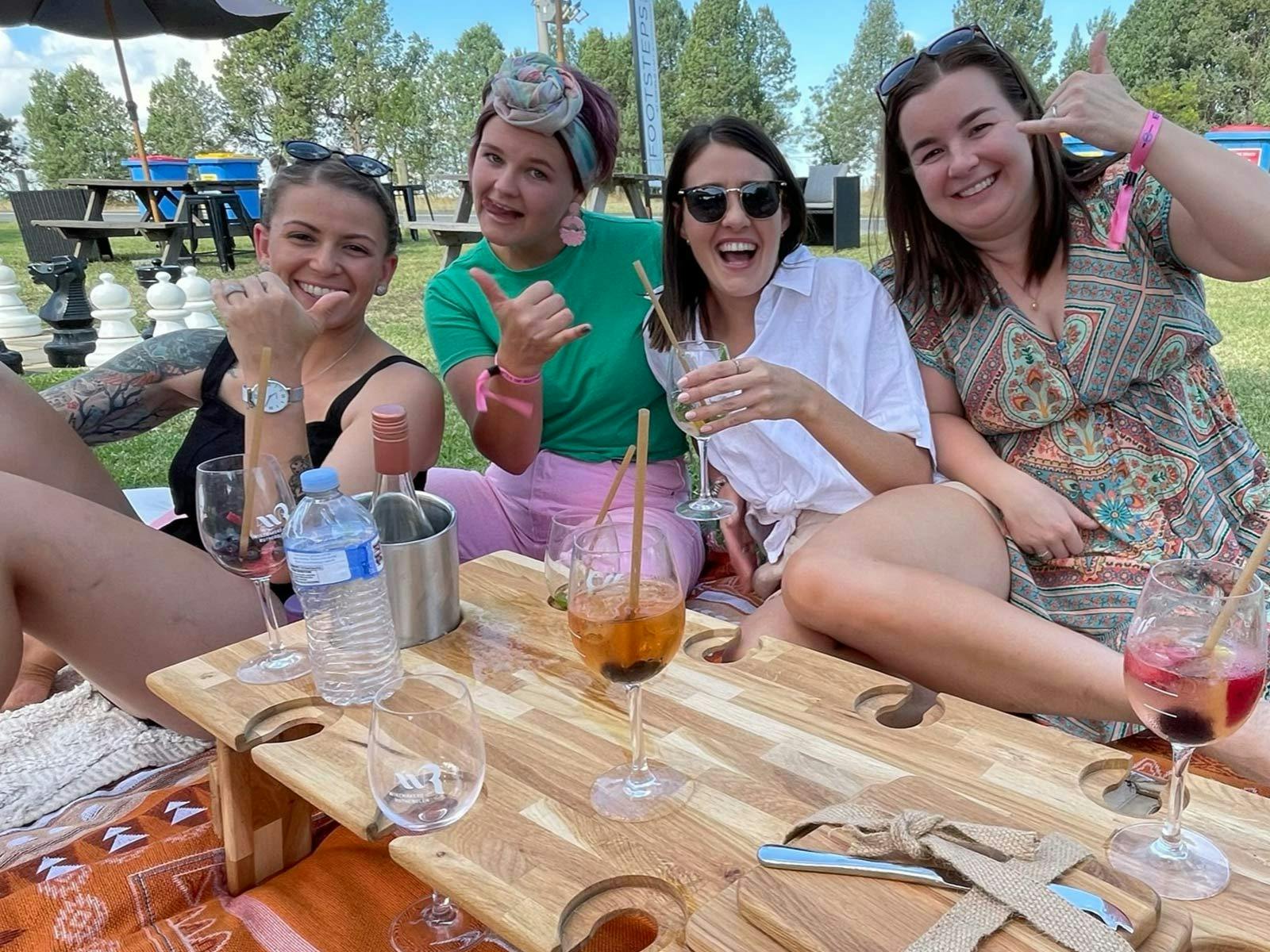Four happy ladies raising their glasses while sitting on a picnic blanket
