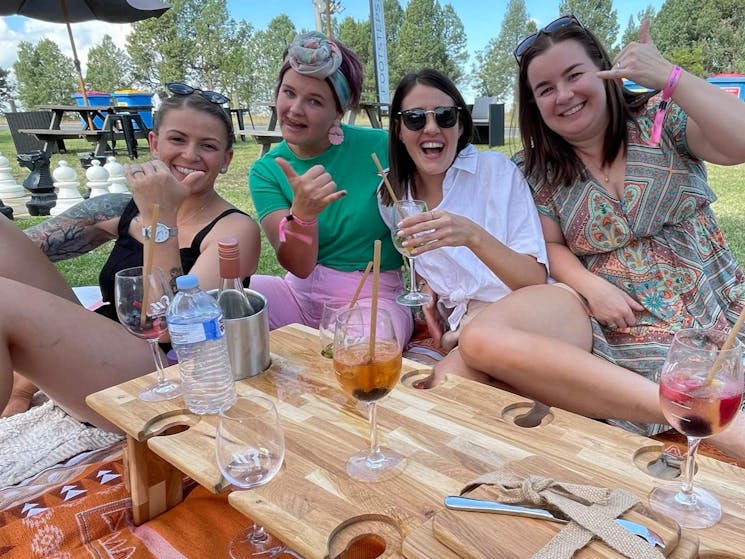 Four happy ladies raising their glasses while sitting on a picnic blanket