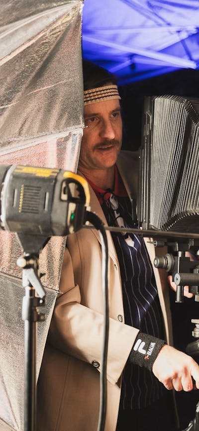 An image of a man setting up a large format camera, surrounded by studio lights