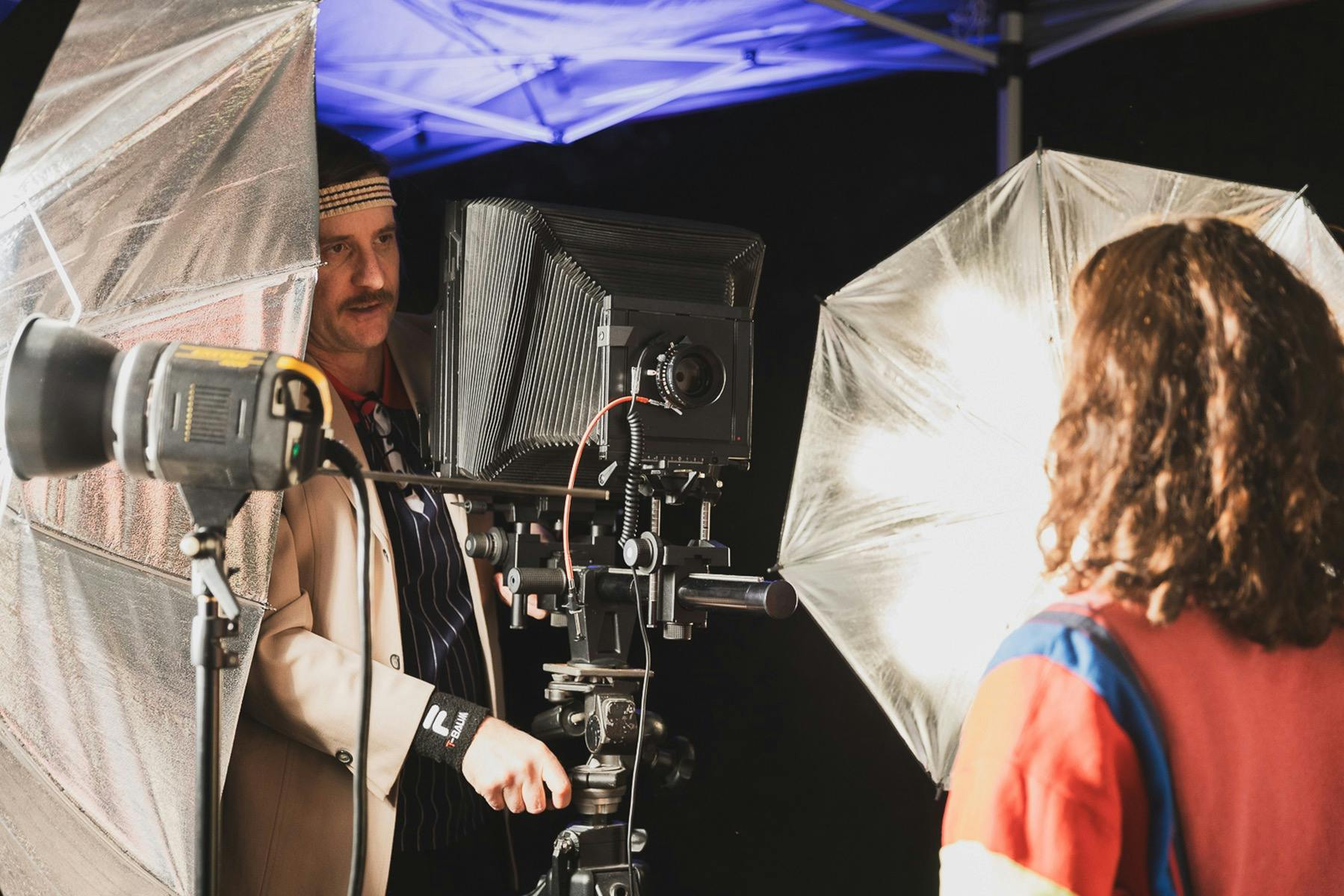 An image of a man setting up a large format camera, surrounded by studio lights