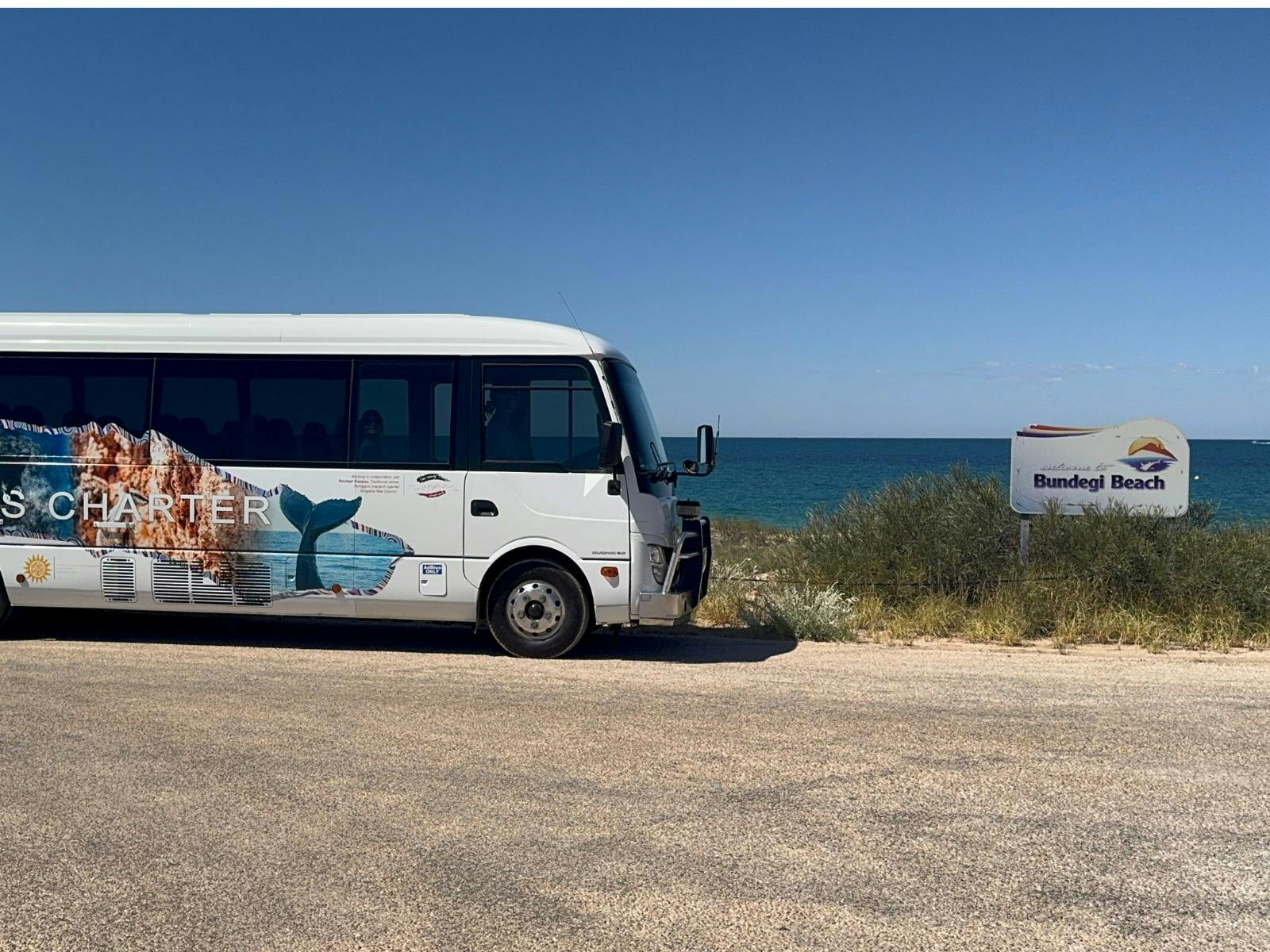 Tour bus at Bundegi Beach with turquoise water and white sand in the background.