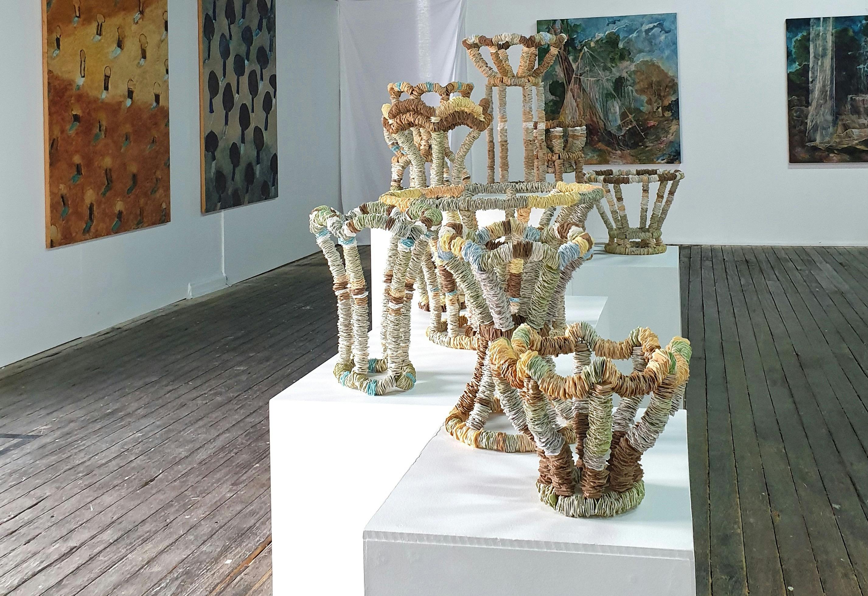 Breadtag sculptures on plinths in front of large paintings