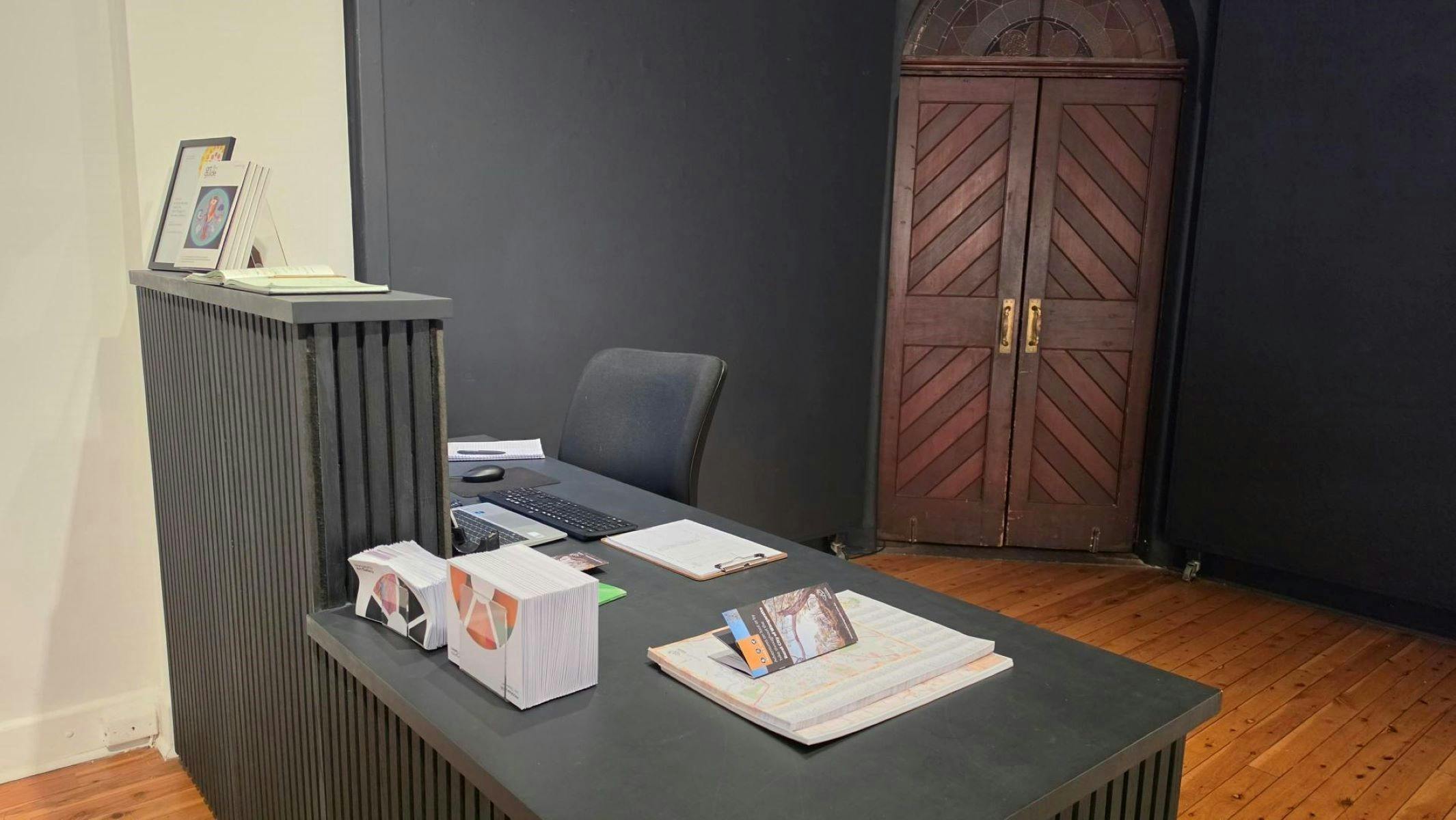 Black desk in front of wooden brown doors, featuring pads of maps
