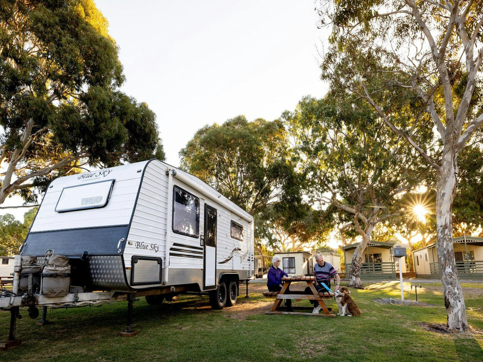 A couple sitting with their pet dog in a Beachside Holiday Parkpowered site.