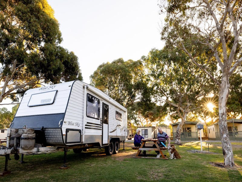 A couple sitting with their pet dog in a Beachside Holiday Parkpowered site.