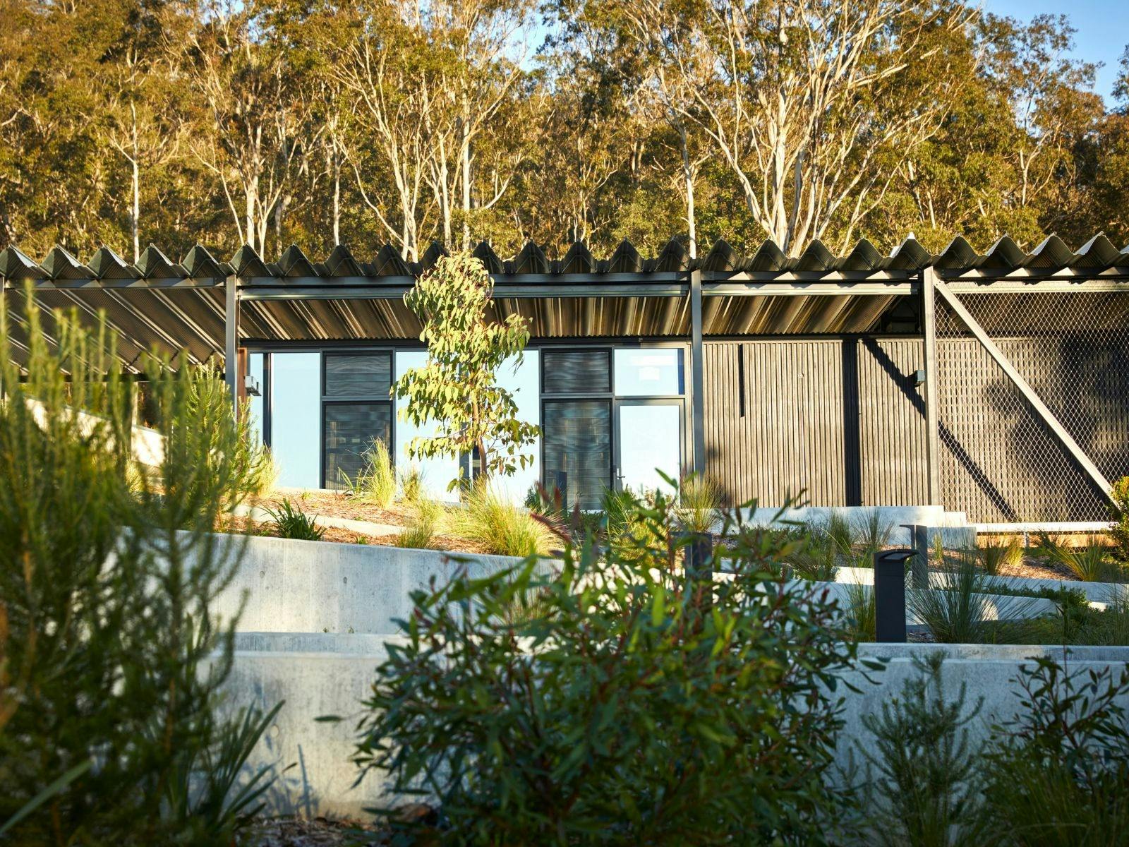 A glass black building with large glass windows behind lush gardens and trees