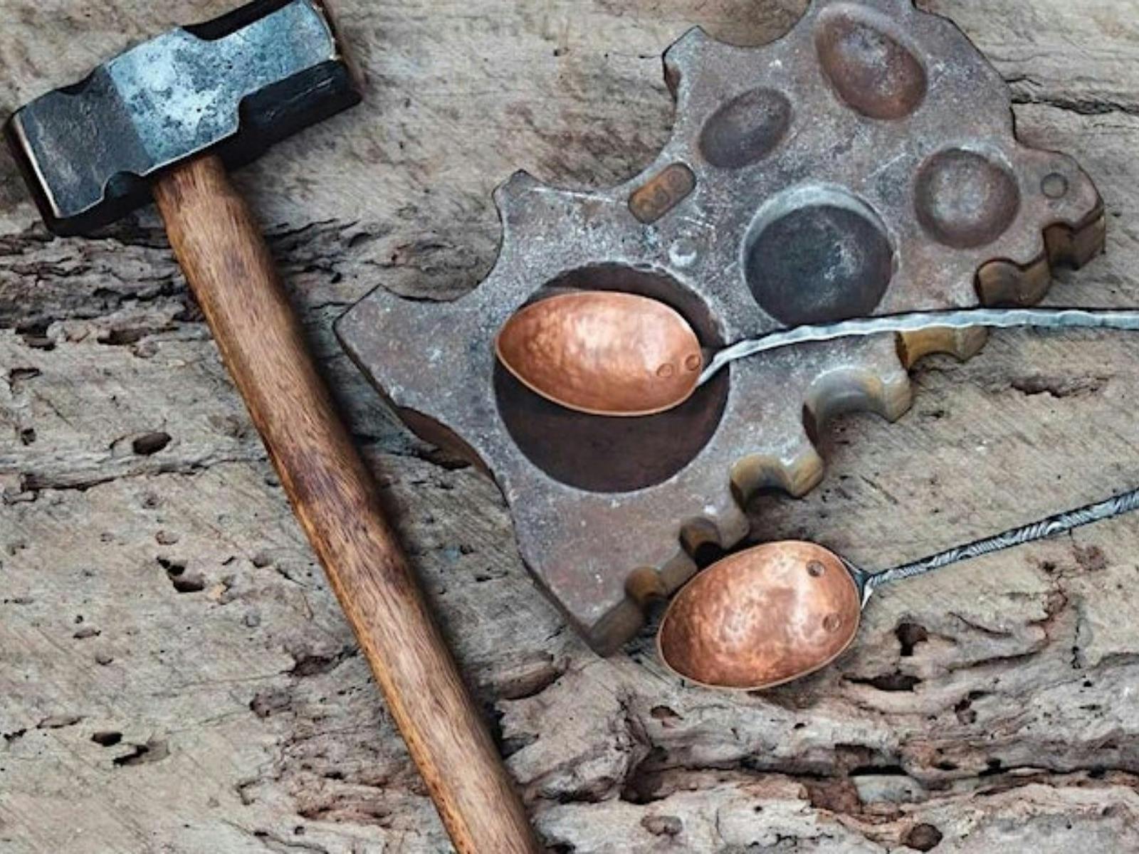 Copper serving utensils resting on bench with hammer