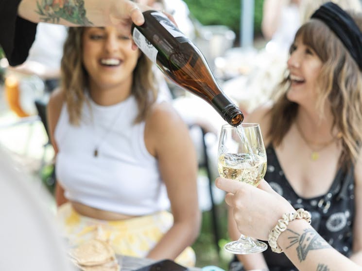 Pouring a glass of wine with two smiling females in the background