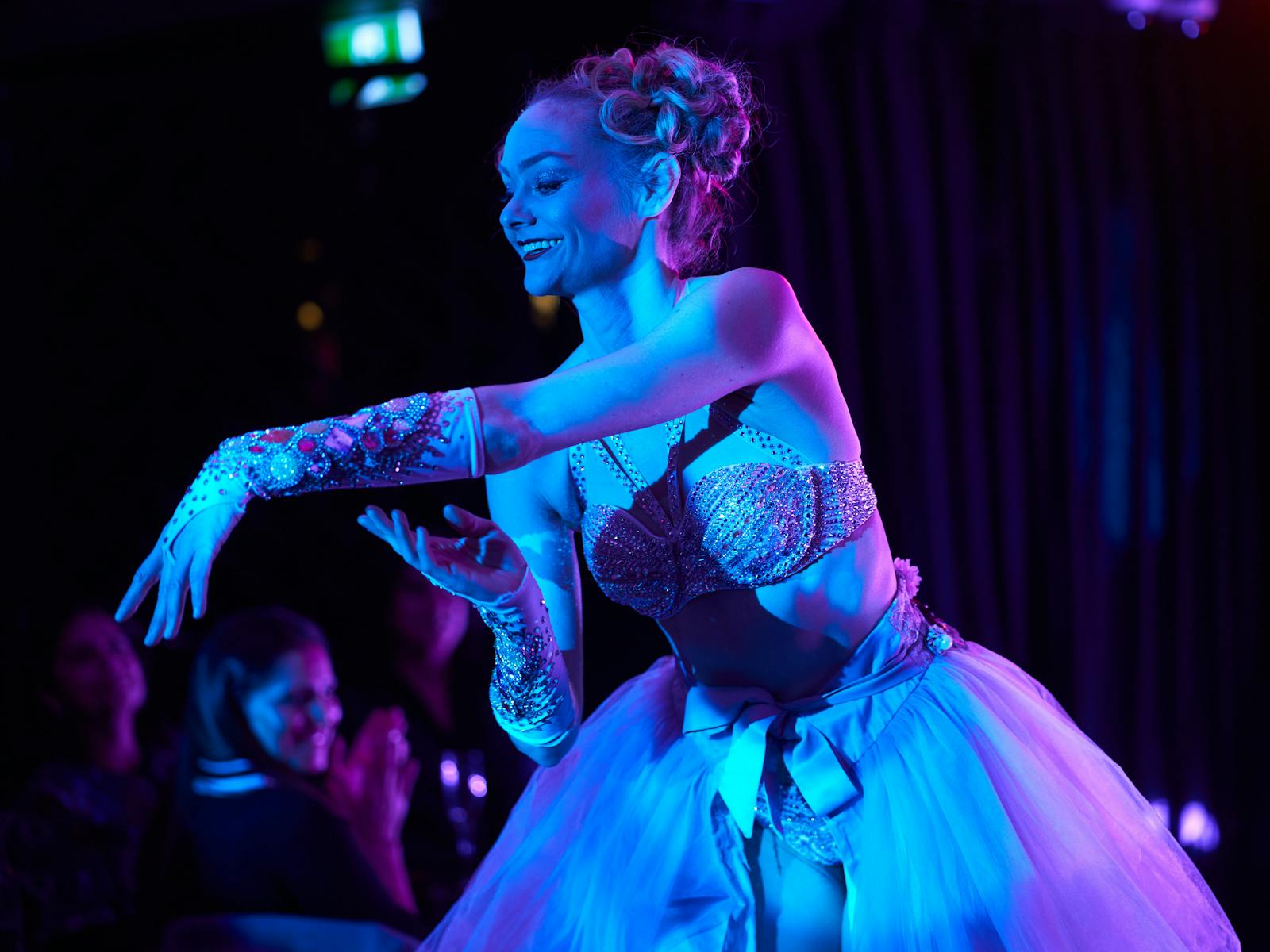 Beautiful ballet dancer smiles while removing glove, under blue stage lights.