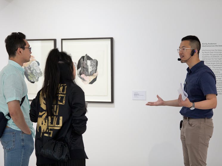 Man talks to young couple in front of framed drawings on the wall