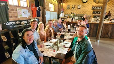 A group of people enjoying wine tasting at a table in a winery's tasting room.