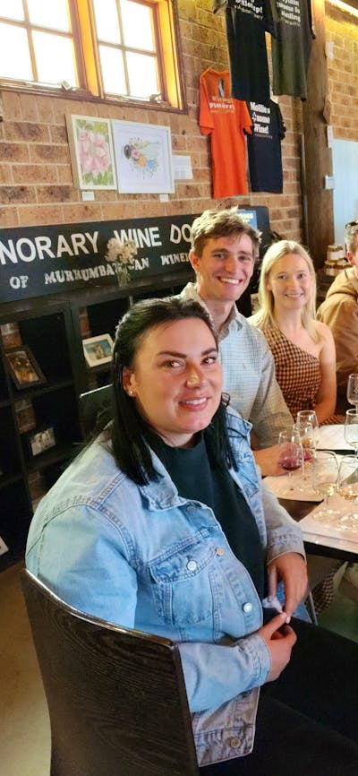 A group of people enjoying wine tasting at a table in a winery's tasting room.