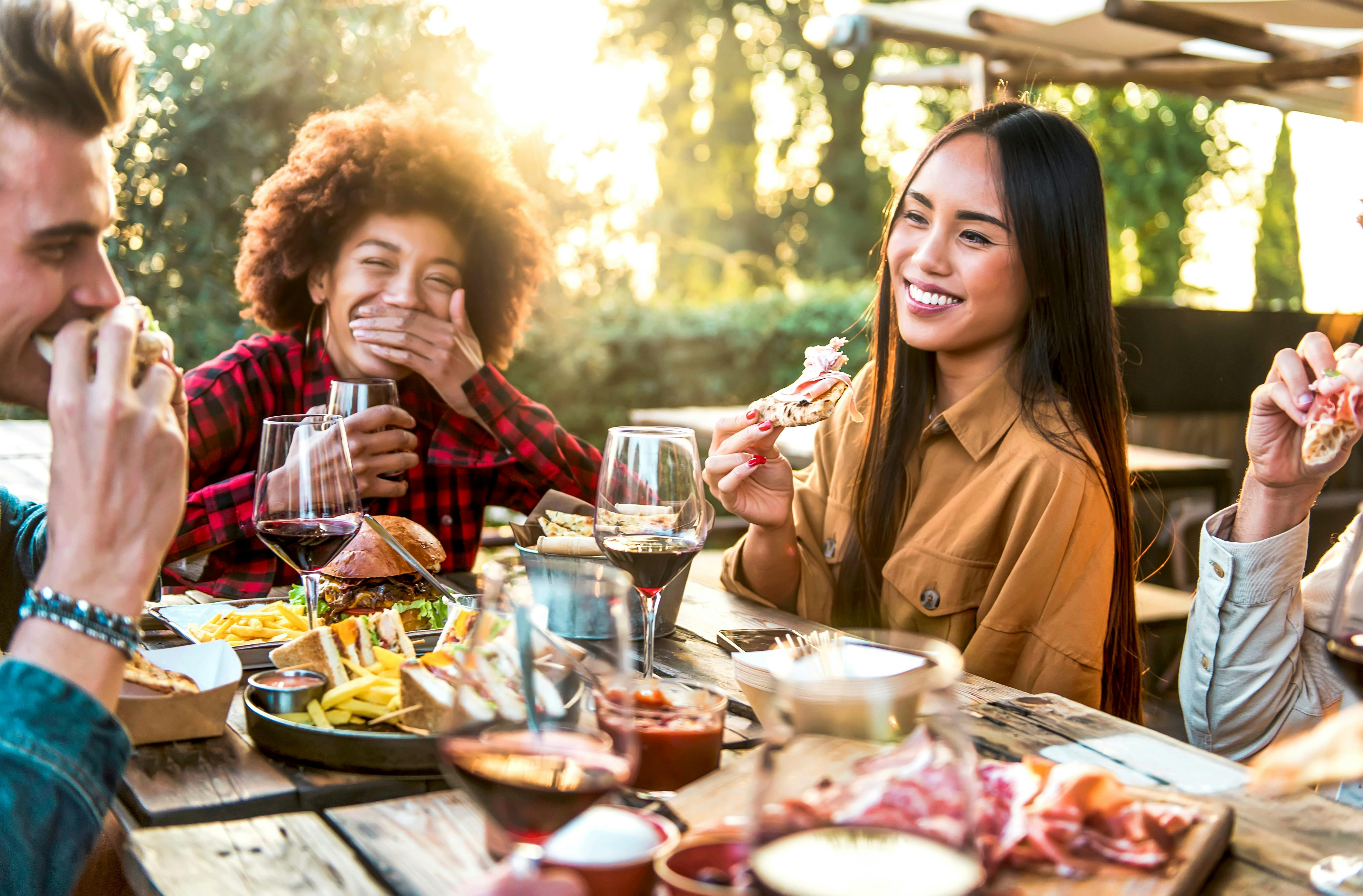 Young group of diverse ethnicity sitting around a table drinking red wine and food